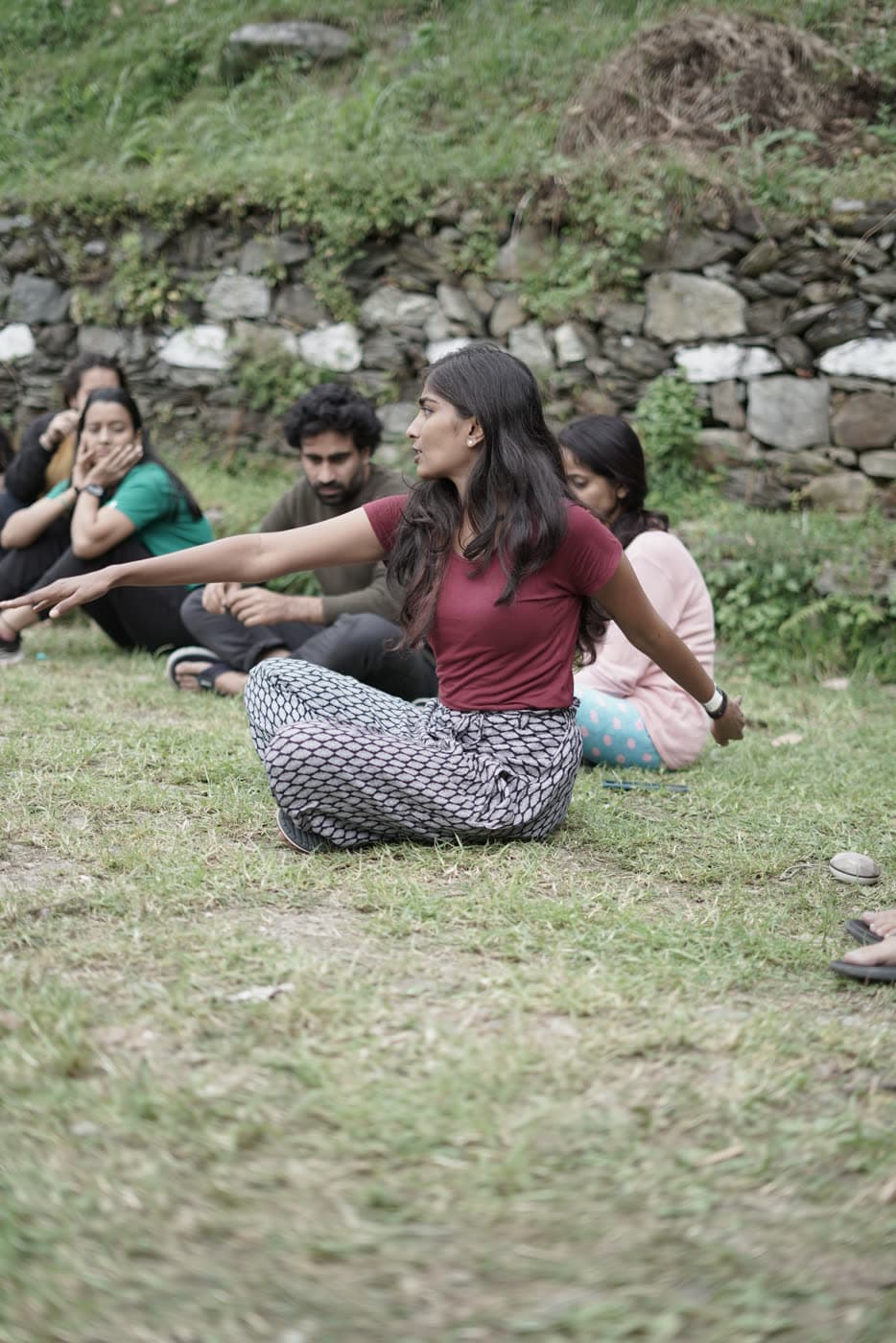 People sitting on a hillside playing a circle game, one of them mid-gesture
